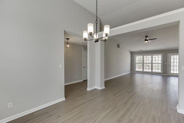 spare room featuring visible vents, light wood-style flooring, ceiling fan with notable chandelier, and baseboards