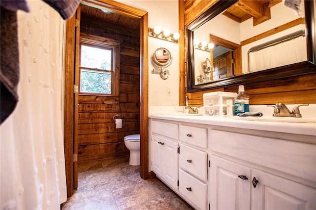 bathroom featuring double vanity, a sink, wooden walls, and toilet