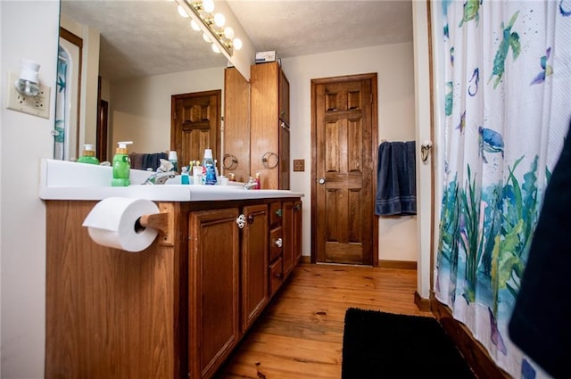 full bath featuring vanity, a textured ceiling, a shower with shower curtain, baseboards, and wood finished floors