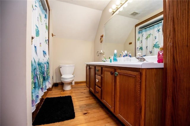 bathroom featuring visible vents, vanity, toilet, wood finished floors, and vaulted ceiling