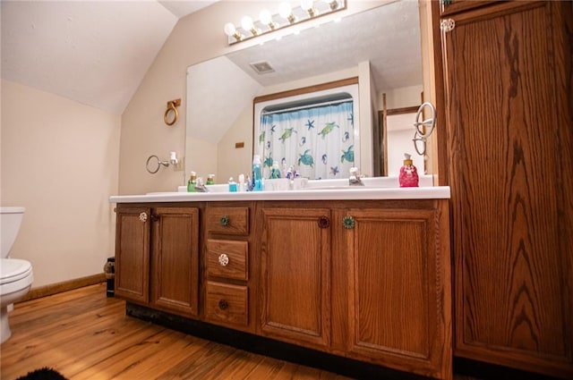 bathroom with vanity, wood finished floors, toilet, baseboards, and vaulted ceiling