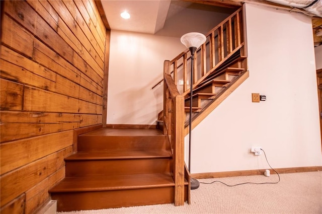 stairway featuring carpet flooring and wooden walls