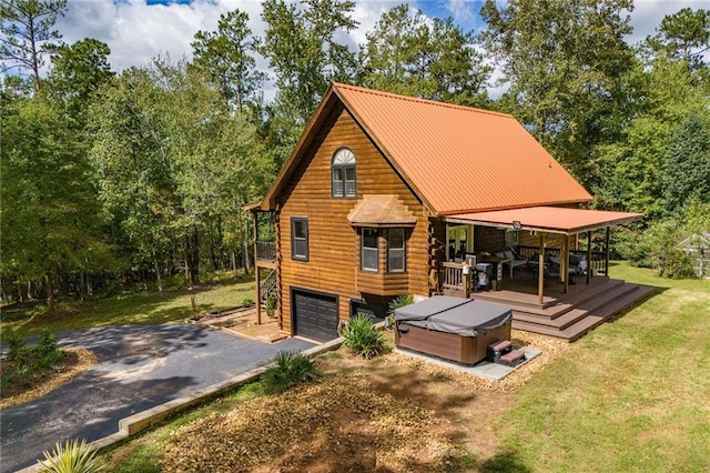 rear view of house with a garage, log exterior, a lawn, a hot tub, and driveway