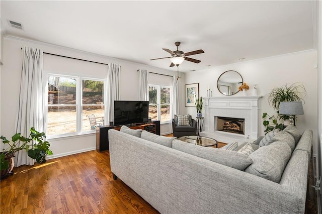 living room with ceiling fan, a tiled fireplace, dark hardwood / wood-style flooring, and crown molding