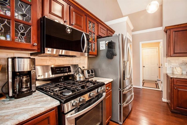 kitchen with decorative backsplash, appliances with stainless steel finishes, light wood-type flooring, light stone countertops, and vaulted ceiling