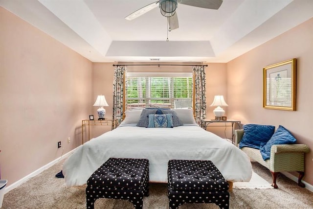 carpeted bedroom with a raised ceiling and ceiling fan