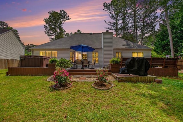 back house at dusk featuring a yard, a hot tub, and a deck