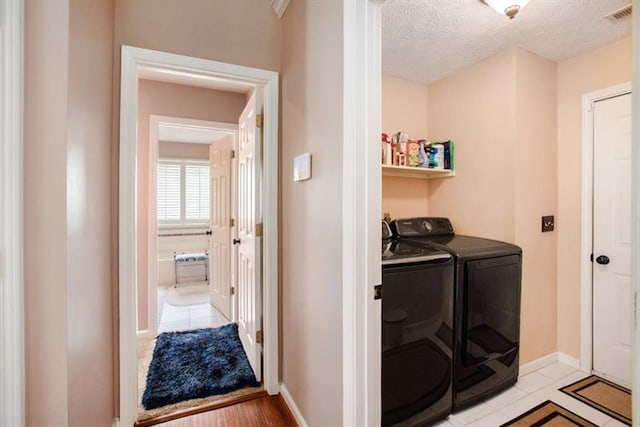 clothes washing area with separate washer and dryer, light hardwood / wood-style flooring, and a textured ceiling