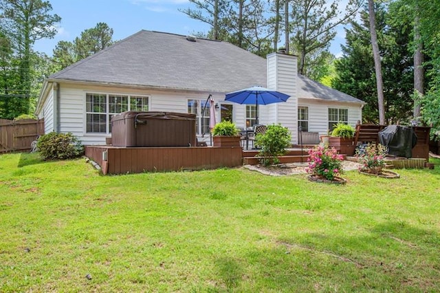 back of house featuring a hot tub, a deck, and a lawn