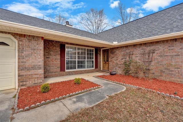 entrance to property with brick siding, roof with shingles, and an attached garage