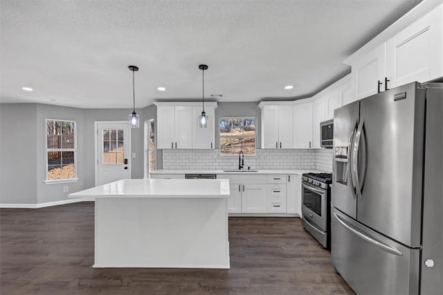 kitchen featuring stainless steel appliances, sink, white cabinets, and decorative light fixtures