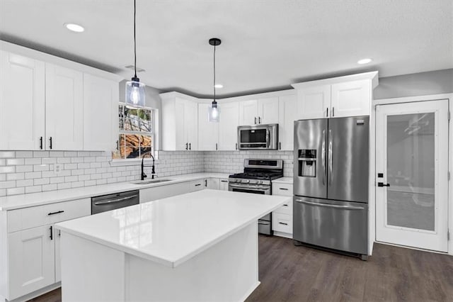 kitchen with sink, hanging light fixtures, stainless steel appliances, white cabinets, and a kitchen island