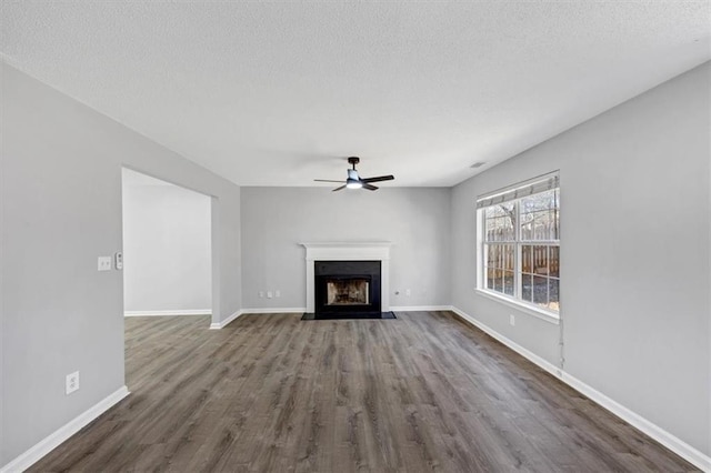 unfurnished living room featuring ceiling fan, dark hardwood / wood-style flooring, and a textured ceiling