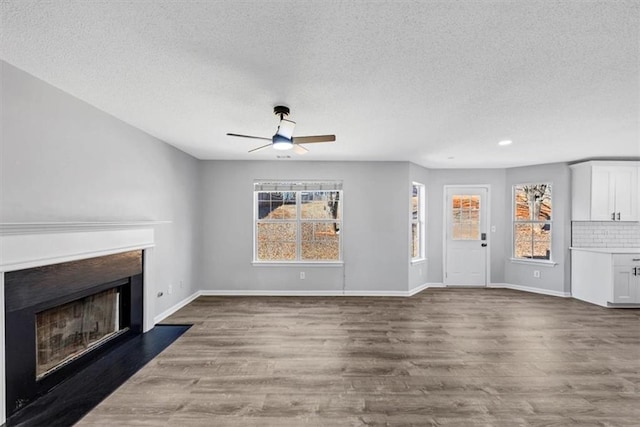 unfurnished living room featuring ceiling fan, a textured ceiling, dark hardwood / wood-style floors, and a healthy amount of sunlight