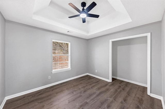 unfurnished bedroom with a tray ceiling, dark hardwood / wood-style floors, and ceiling fan