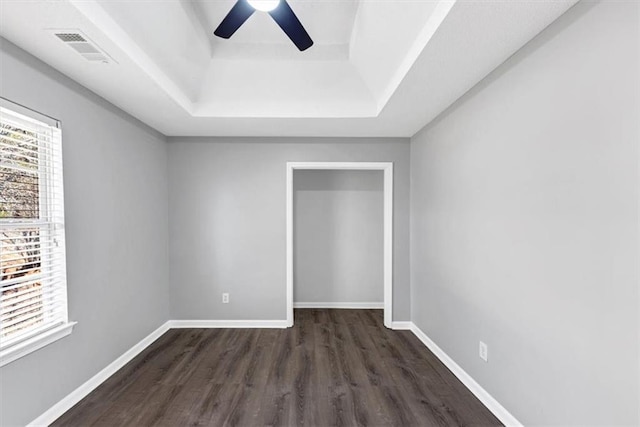 spare room with dark wood-type flooring, ceiling fan, and a raised ceiling