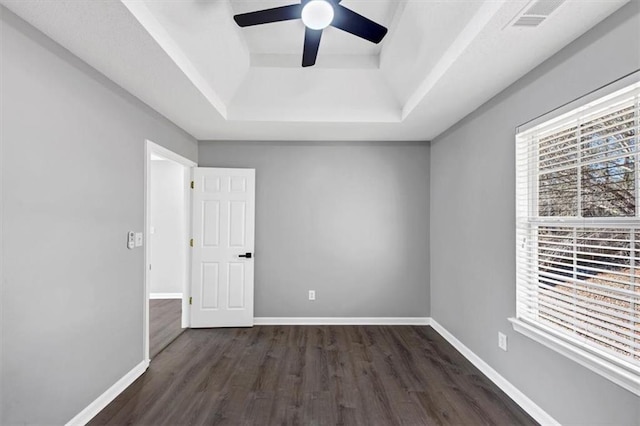 unfurnished room featuring a raised ceiling, dark wood-type flooring, and ceiling fan