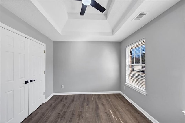 unfurnished bedroom featuring a tray ceiling, dark wood-type flooring, a closet, and ceiling fan