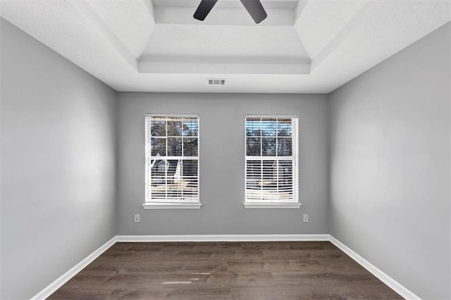 unfurnished room with plenty of natural light, dark wood-type flooring, and a tray ceiling