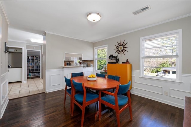 dining space with ornamental molding, a wainscoted wall, visible vents, and wood finished floors