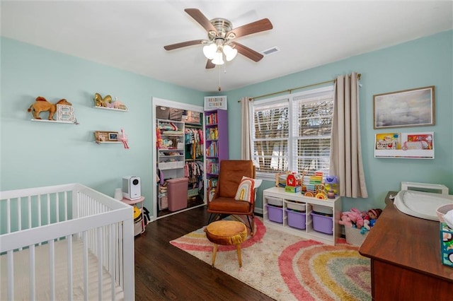 bedroom with ceiling fan, wood finished floors, visible vents, a closet, and a crib