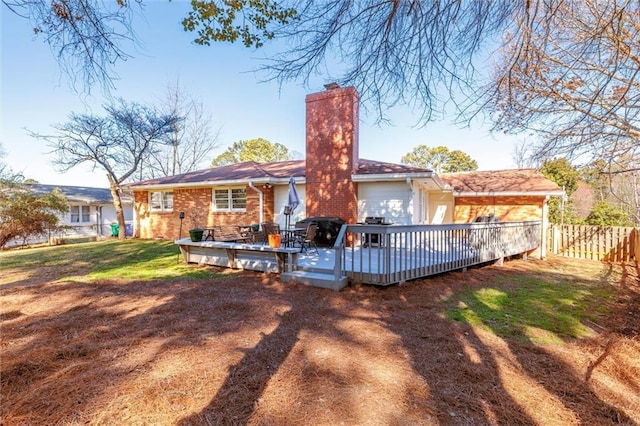 rear view of house with a deck, brick siding, fence, a yard, and a chimney