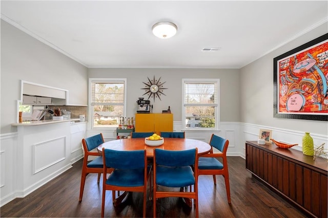 dining area featuring dark wood-style floors, visible vents, a wainscoted wall, and ornamental molding