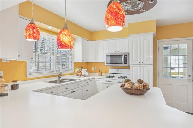 kitchen with white range with gas stovetop, stainless steel microwave, decorative light fixtures, white cabinetry, and a sink