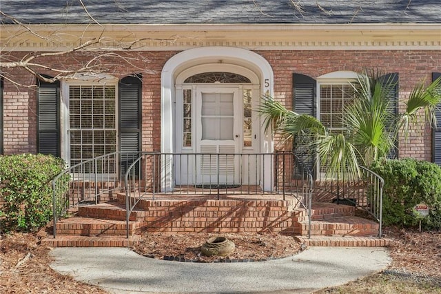 property entrance with a shingled roof and brick siding