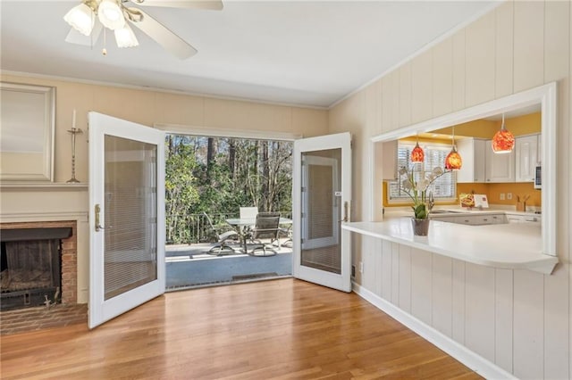 doorway to outside with light wood finished floors, a fireplace, a ceiling fan, and crown molding