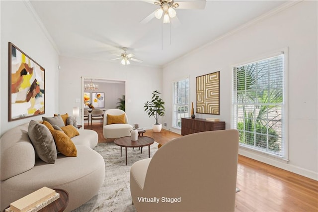 living area with ceiling fan with notable chandelier, light wood finished floors, a wealth of natural light, and crown molding