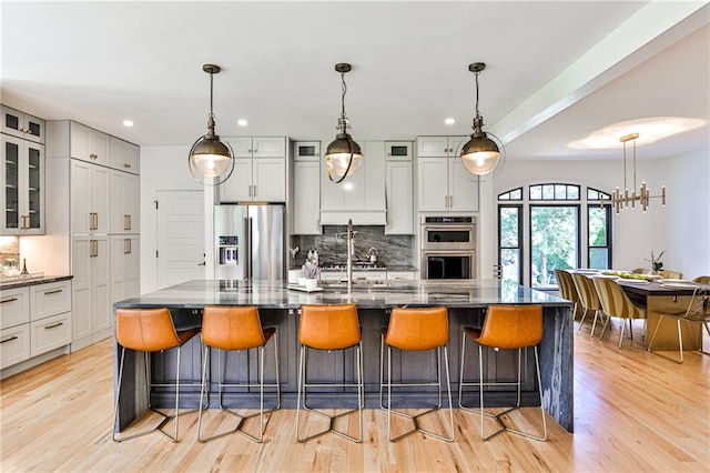 kitchen featuring stainless steel appliances, a kitchen bar, backsplash, a large island with sink, and dark stone countertops