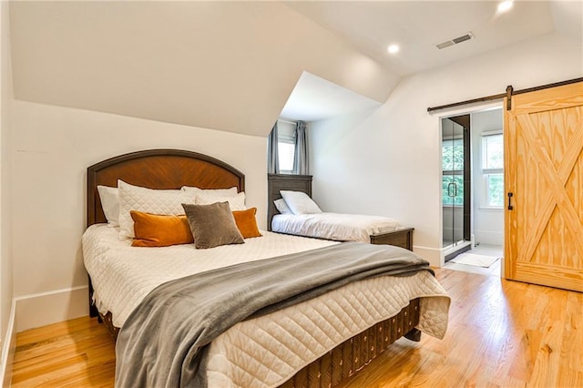 bedroom with ensuite bath, hardwood / wood-style flooring, vaulted ceiling, and a barn door