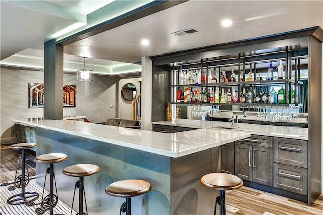 bar with light wood-type flooring, pendant lighting, and light stone countertops