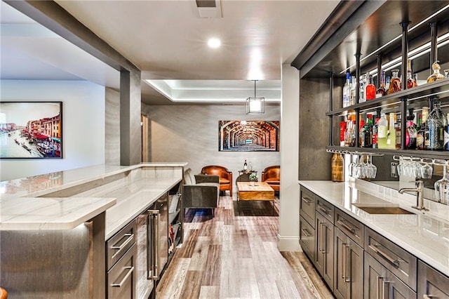 bar featuring light hardwood / wood-style floors, hanging light fixtures, light stone counters, sink, and dark brown cabinets