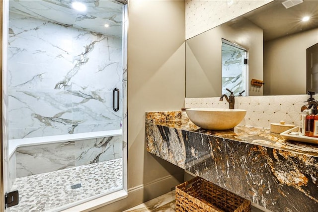 bathroom with a shower with shower door, decorative backsplash, and sink