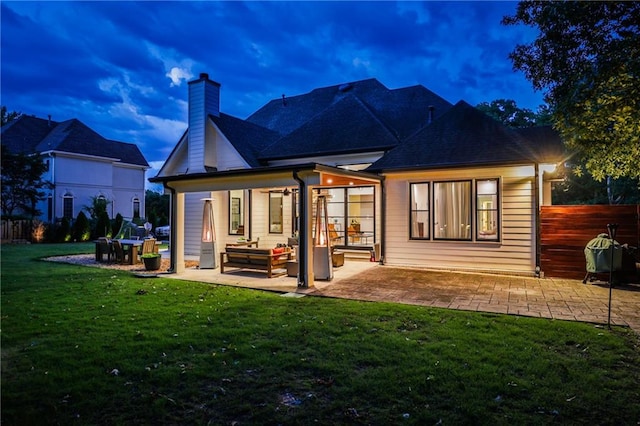 back house at dusk featuring a patio area, outdoor lounge area, and a yard