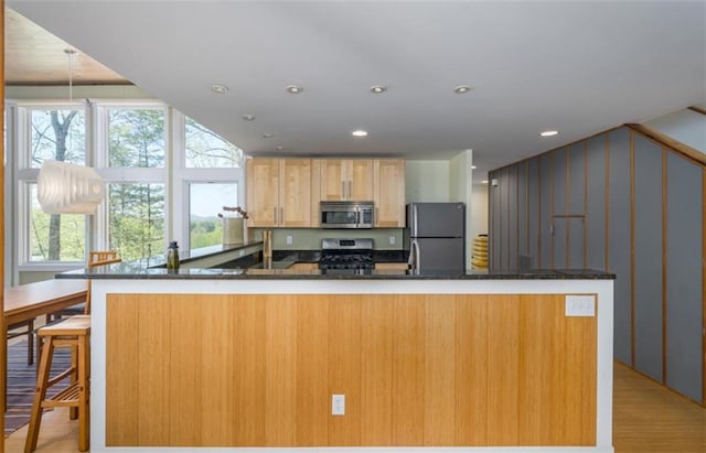 kitchen featuring recessed lighting, a peninsula, dark stone countertops, light wood-style floors, and appliances with stainless steel finishes