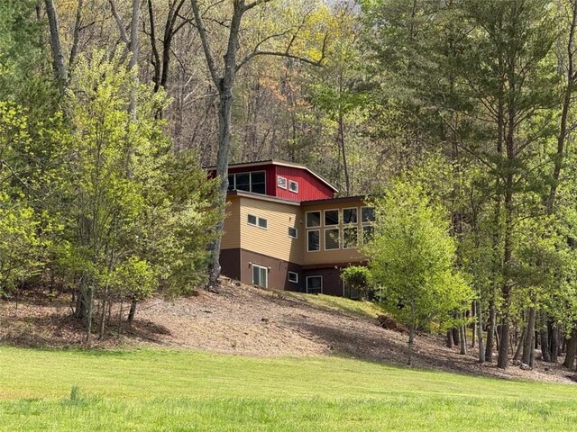 rear view of house featuring a forest view and a lawn