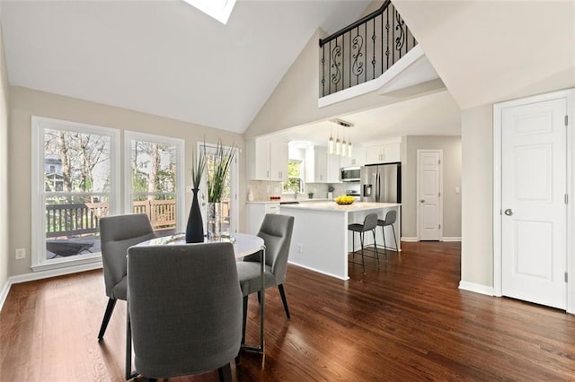 dining room with a skylight, dark wood-style floors, baseboards, and high vaulted ceiling