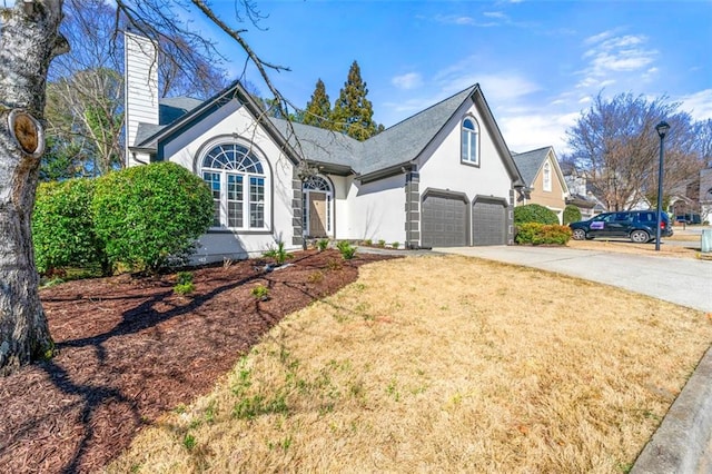 view of front of house with concrete driveway, a front yard, stucco siding, a chimney, and a garage