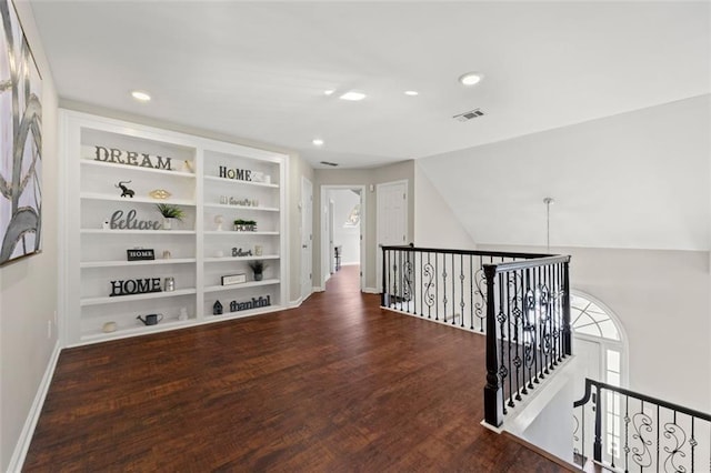 hallway featuring an upstairs landing, visible vents, built in shelves, and wood finished floors