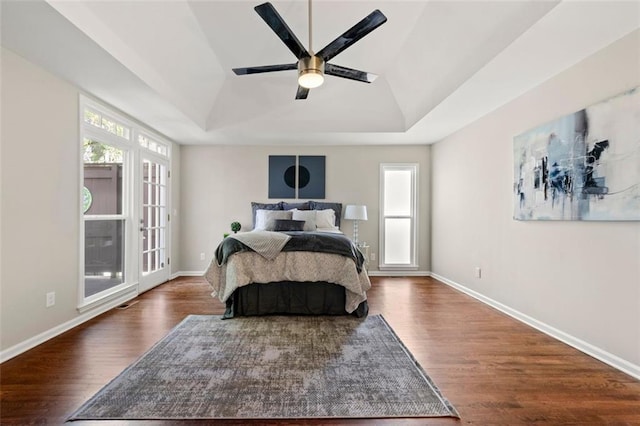 bedroom with multiple windows, a raised ceiling, baseboards, and wood finished floors