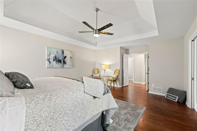 bedroom with visible vents, ceiling fan, baseboards, dark wood-style floors, and a raised ceiling