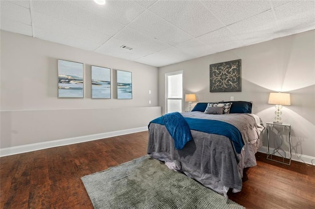 bedroom with visible vents, a paneled ceiling, baseboards, and wood finished floors