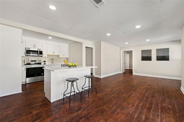 kitchen with visible vents, a kitchen island, a breakfast bar, decorative backsplash, and appliances with stainless steel finishes