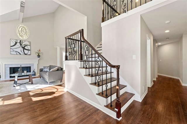 staircase with a premium fireplace, a towering ceiling, baseboards, and wood finished floors