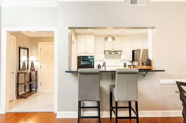 211 Colonial Homes Dr NW Unit 2501, Atlanta, GA 30309 - kitchen with oven, a kitchen bar, backsplash, freestanding refrigerator, and white cabinetry
