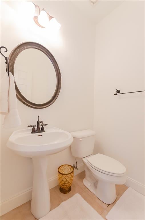 half bath featuring toilet, baseboards, a sink, and tile patterned floors