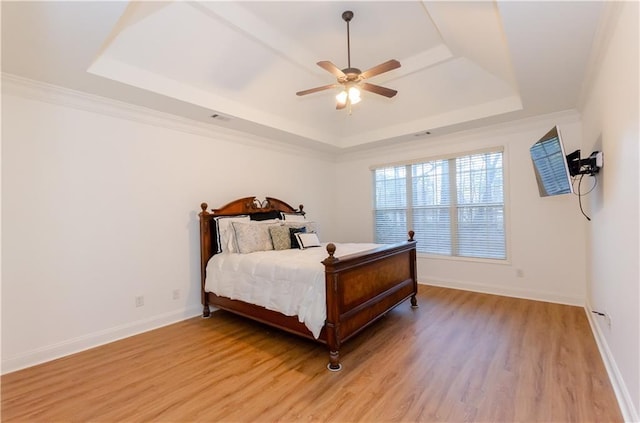 bedroom with ceiling fan, baseboards, light wood-type flooring, a raised ceiling, and crown molding